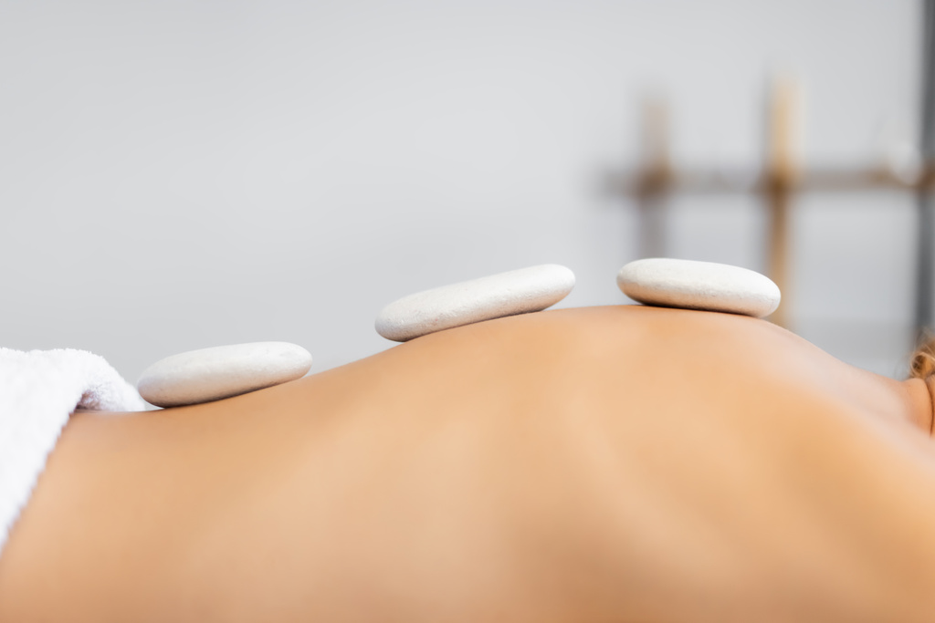 bijgesneden uitzicht op vrouw ontvangen hete steen massage in spa centrum  - Foto, afbeelding