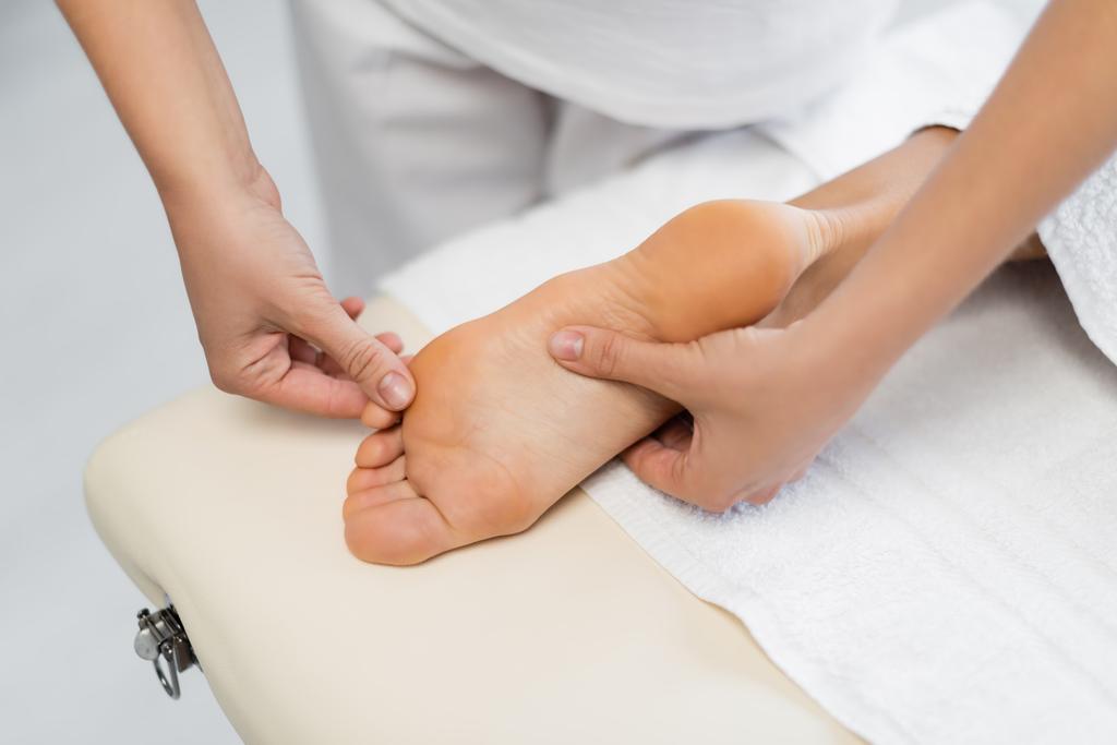 vista ad alto angolo del massaggiatore professionista che fa massaggio ai piedi al cliente nel centro benessere  - Foto, immagini