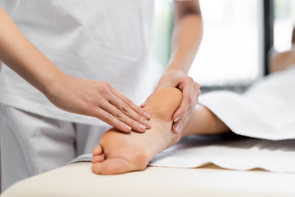 vista cortada de massagista fazendo massagem nos pés para cliente desfocado no centro de spa  - Foto, Imagem