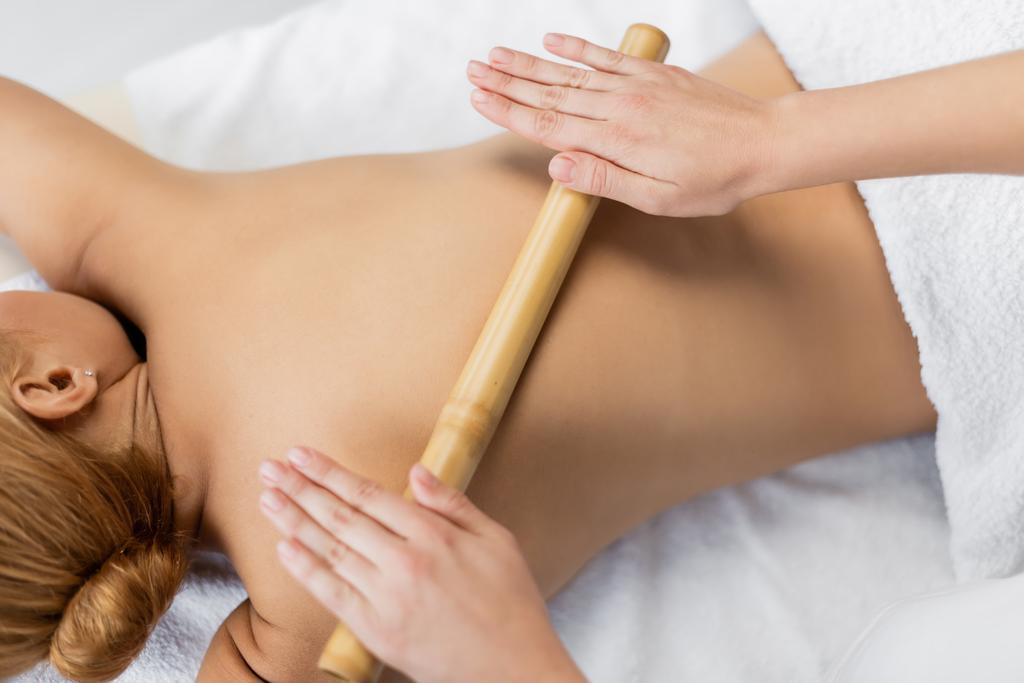 bovenaanzicht van professionele masseur masseren rug van cliënt met bamboe stick - Foto, afbeelding