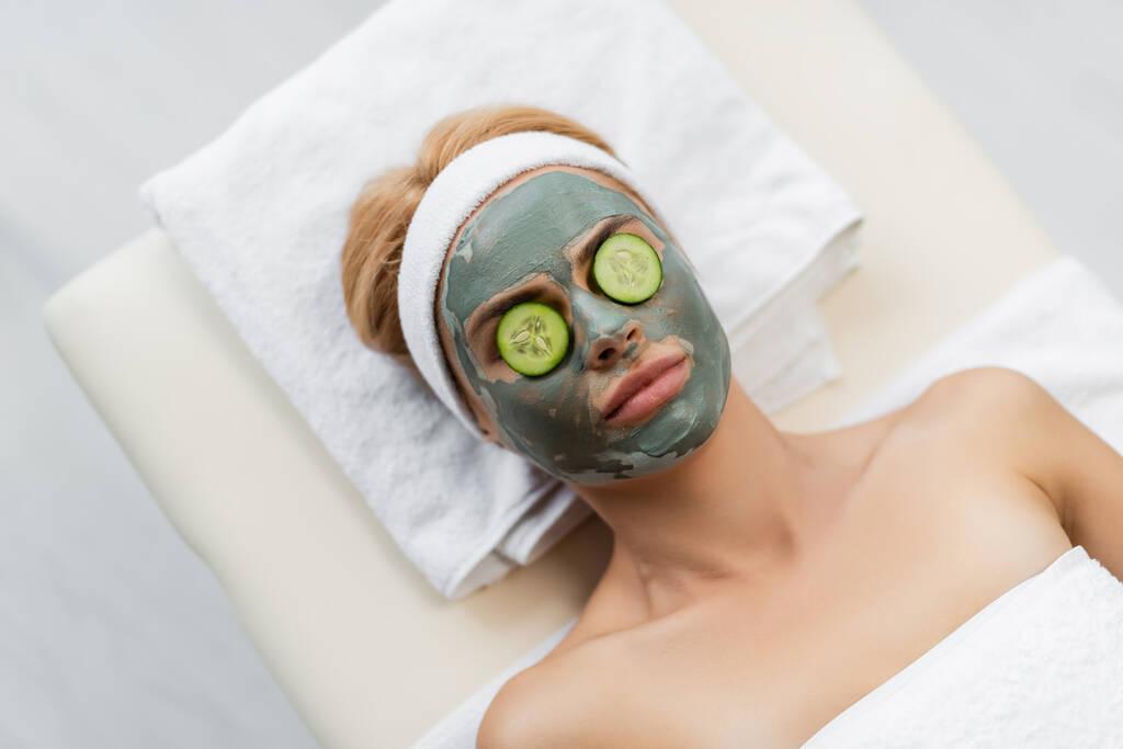 vue de dessus de la femme avec masque en argile et tranches de concombre frais sur les yeux couchés sur la table de massage - Photo, image