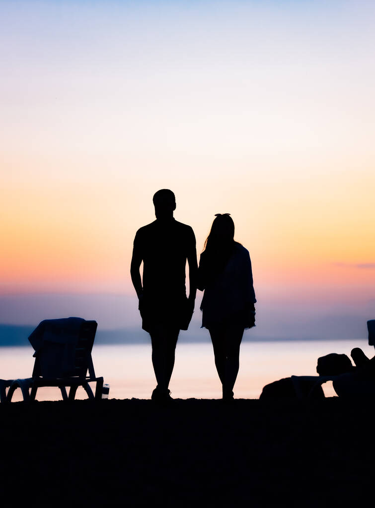 Egy fiatal pár sziluettje áll a parton, a Sevan-tónál a háttérben naplementekor. - Fotó, kép
