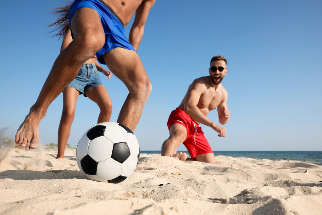 Группа друзей играет в футбол на пляже - Фото, изображение