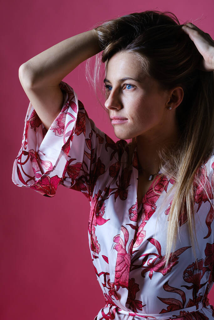 A vertical shot of an attractive Caucasian female wearing a beautiful shirt posing against a pink wall - Photo, Image