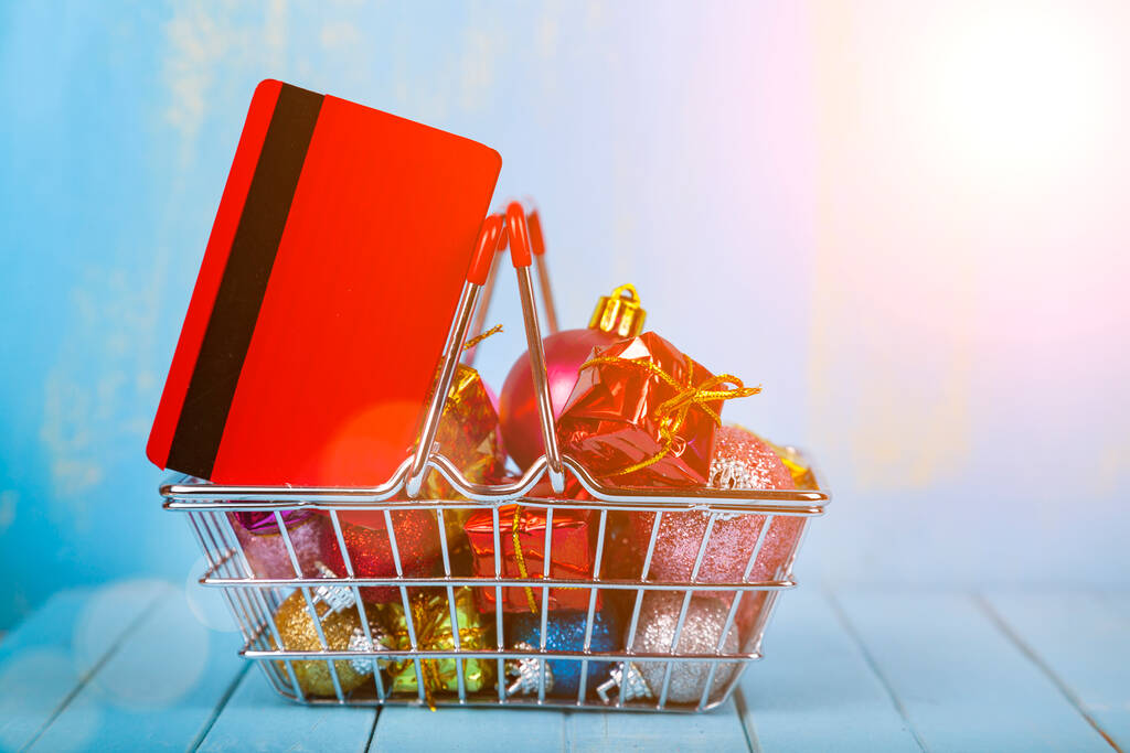 Cesta de la compra con regalos de Navidad, decoración y tarjeta de crédito sobre un fondo de madera azul. Venta de Navidad. - Foto, imagen