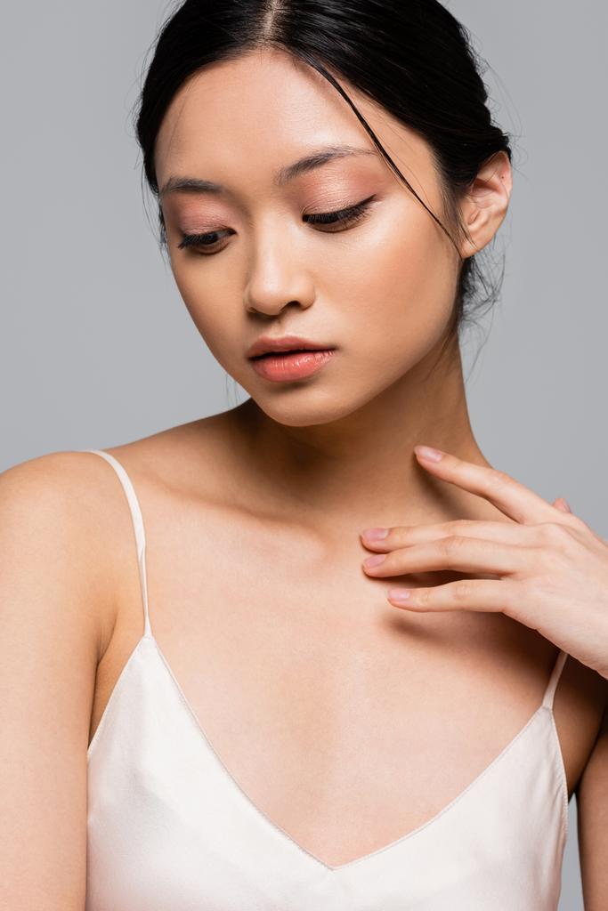 Asiatin mit perfekter Haut, die Brust berührt, isoliert auf grau  - Foto, Bild