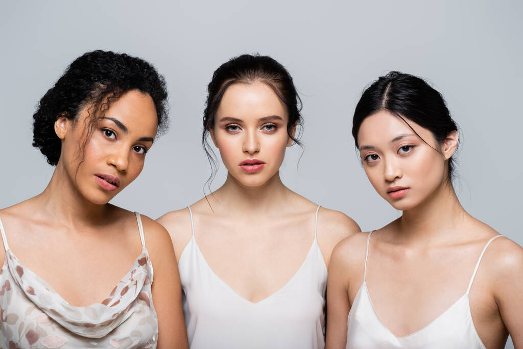 Pretty multiethnic women with perfect skin looking at camera isolated on grey  - Photo, Image