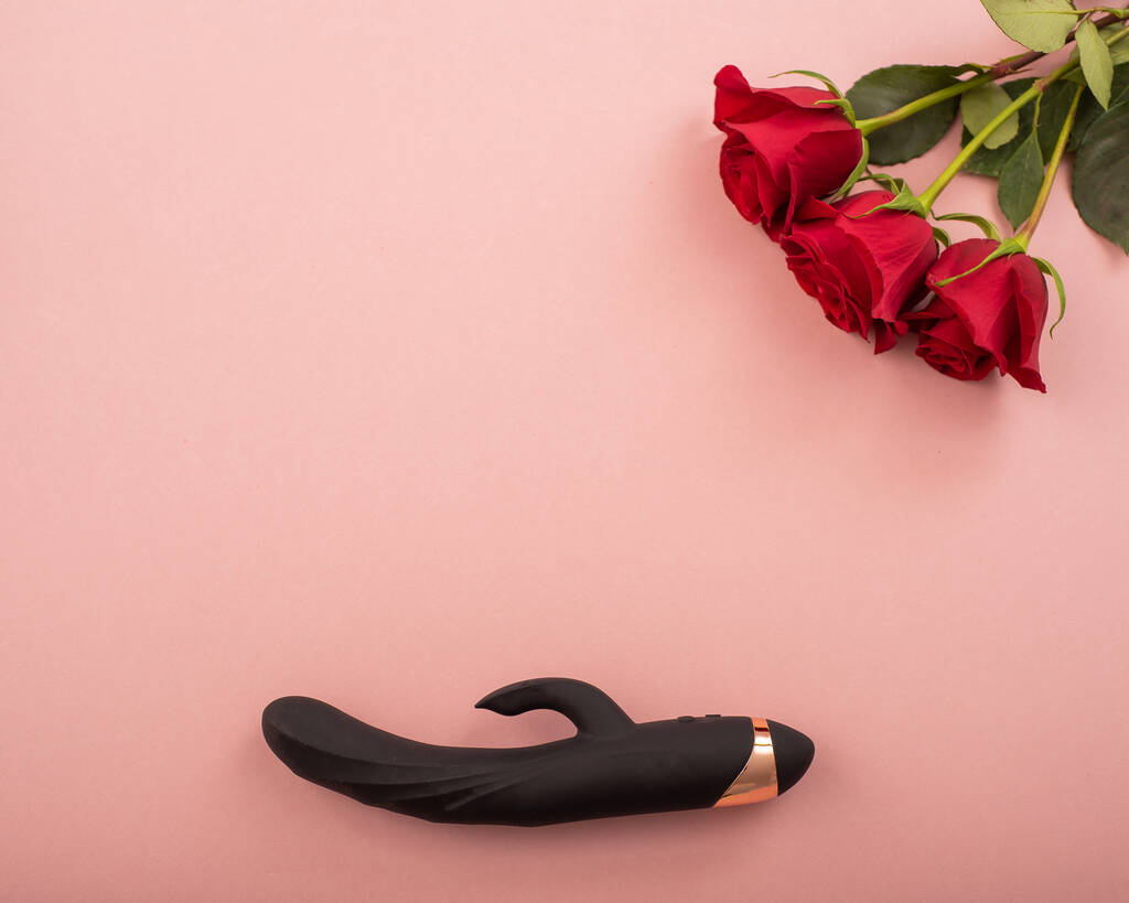 Top view of a black dildo and a bouquet of scarlet roses on a pink background. Copy space - Foto, Bild