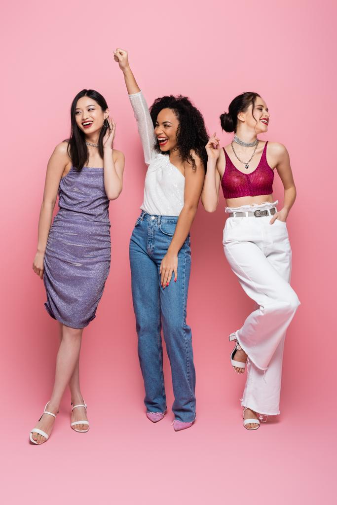 Volle Länge glücklicher multikultureller Frauen, die während einer Party auf rosa Hintergrund posieren - Foto, Bild