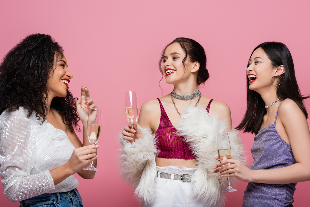 Sorrindo e elegante interracial mulheres segurando champanhe e falando isolado em rosa  - Foto, Imagem