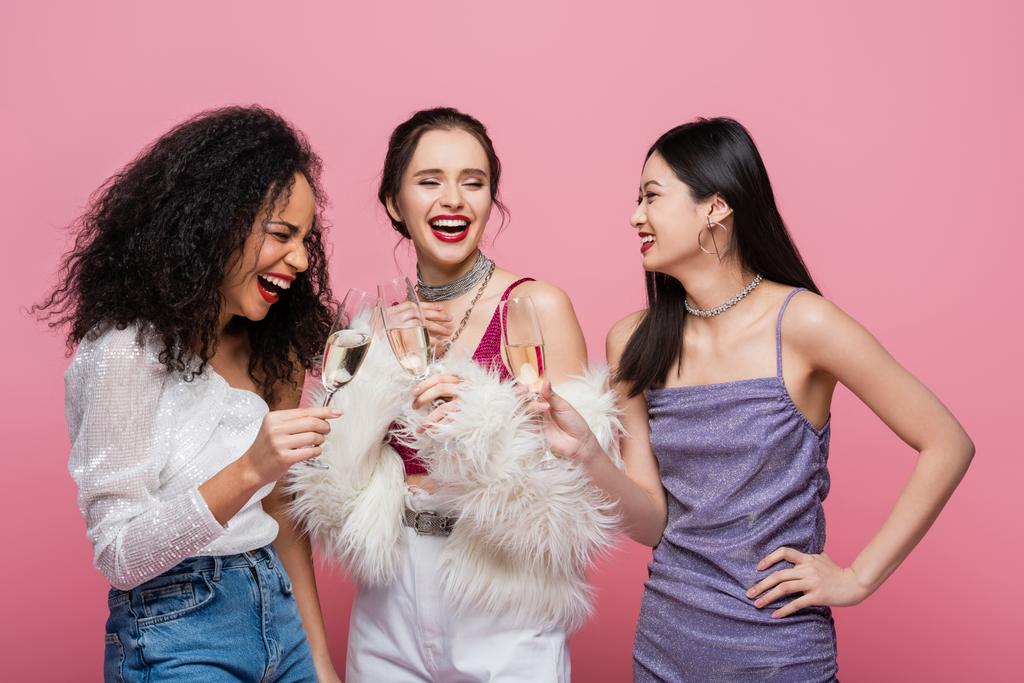 Riendo amigos multiculturales sosteniendo champán durante la fiesta aislado en rosa  - Foto, imagen