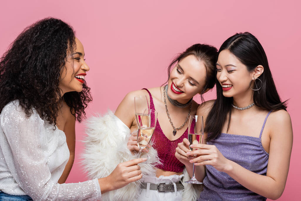 Ładna Afroamerykanka trzymająca szampana w pobliżu uśmiechniętych, międzyrasowych przyjaciół odizolowanych na różowo  - Zdjęcie, obraz