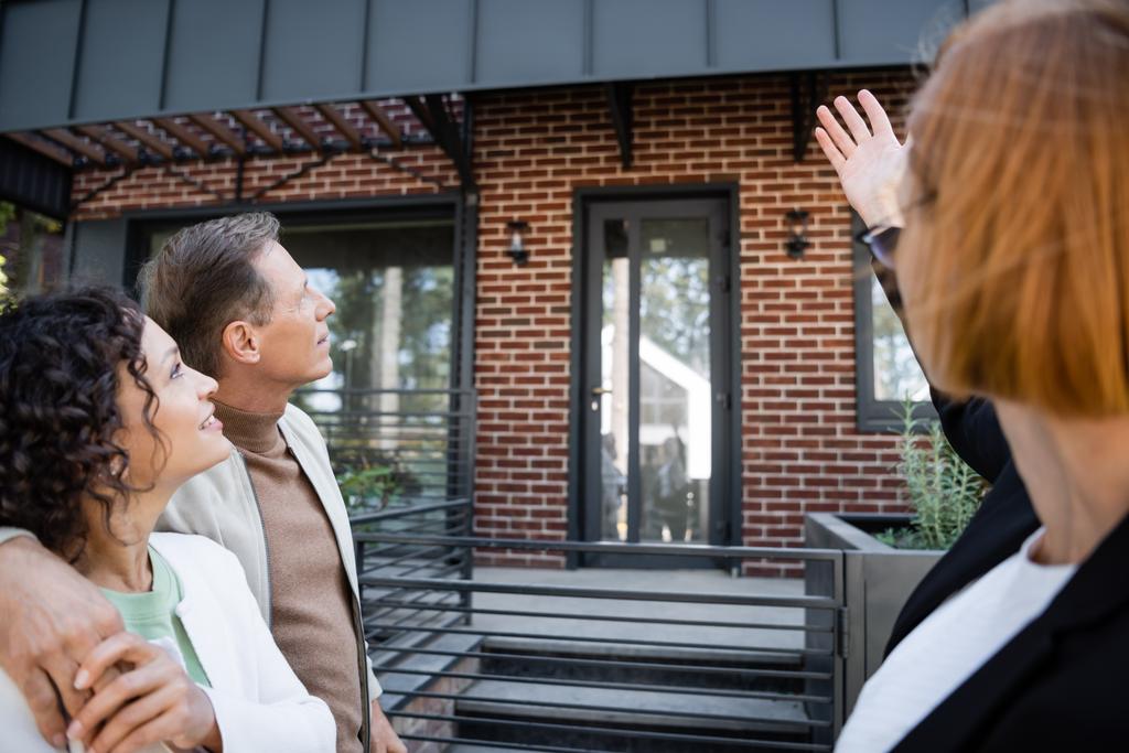 rousse floue agent immobilier pointant vers la maison près marié couple interracial - Photo, image