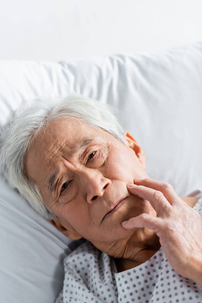 Ältere asiatische Patientin schaut in Kamera, während sie in der Klinik auf dem Bett liegt  - Foto, Bild