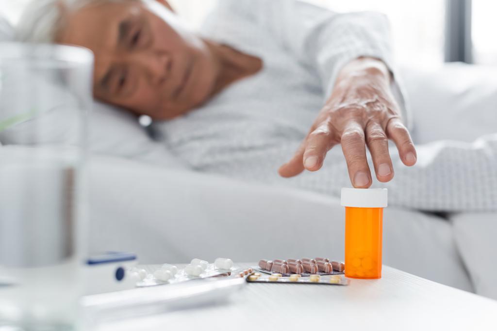 Homályos ázsiai beteg tablettákat szed víz közelében a kórházi kórteremben  - Fotó, kép