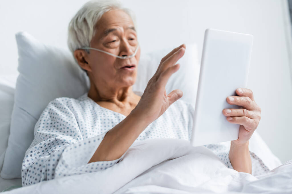 Цифровой планшет в руке размытого азиатского пациента с носовым канюлем в больничном отделении  - Фото, изображение