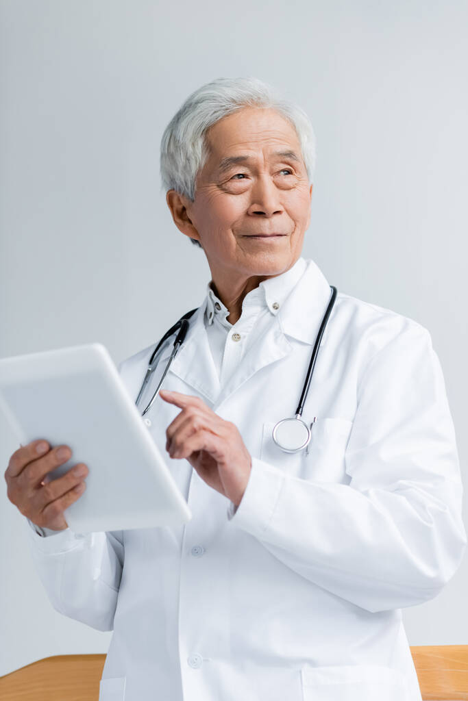 病院でデジタルタブレットを保持白いコートのシニアアジアの医師  - 写真・画像