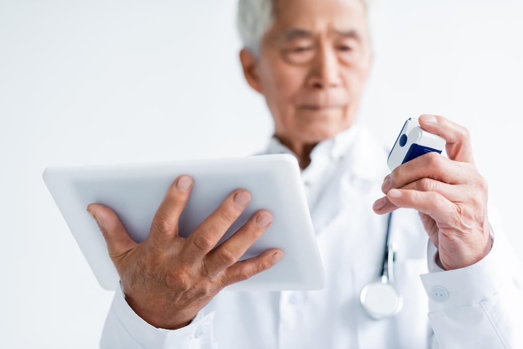 Laptop und Pulsoximeter in den Händen verschwommener asiatischer Arzt in Klinik  - Foto, Bild