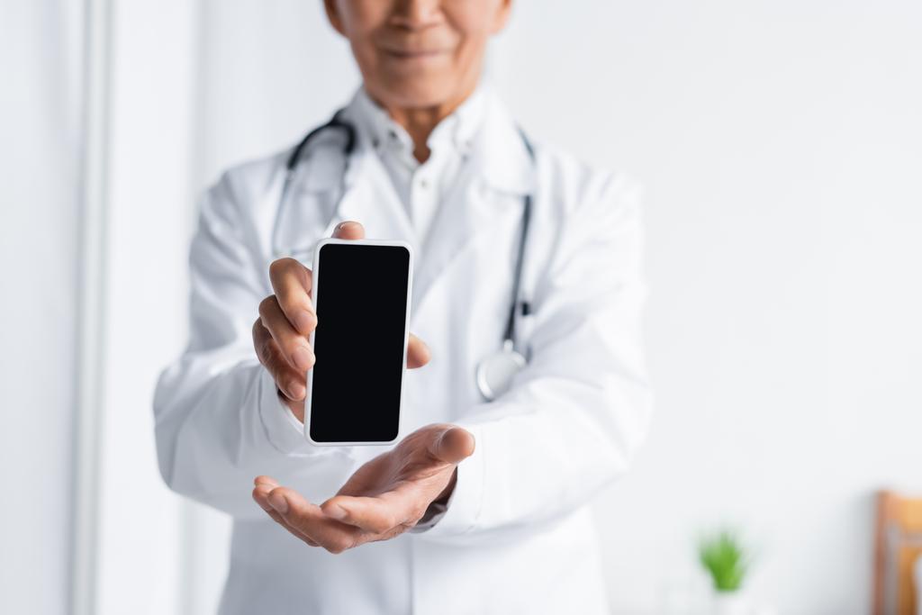 Καλλιεργημένη άποψη του smartphone στα χέρια του θολή γιατρό στην κλινική  - Φωτογραφία, εικόνα