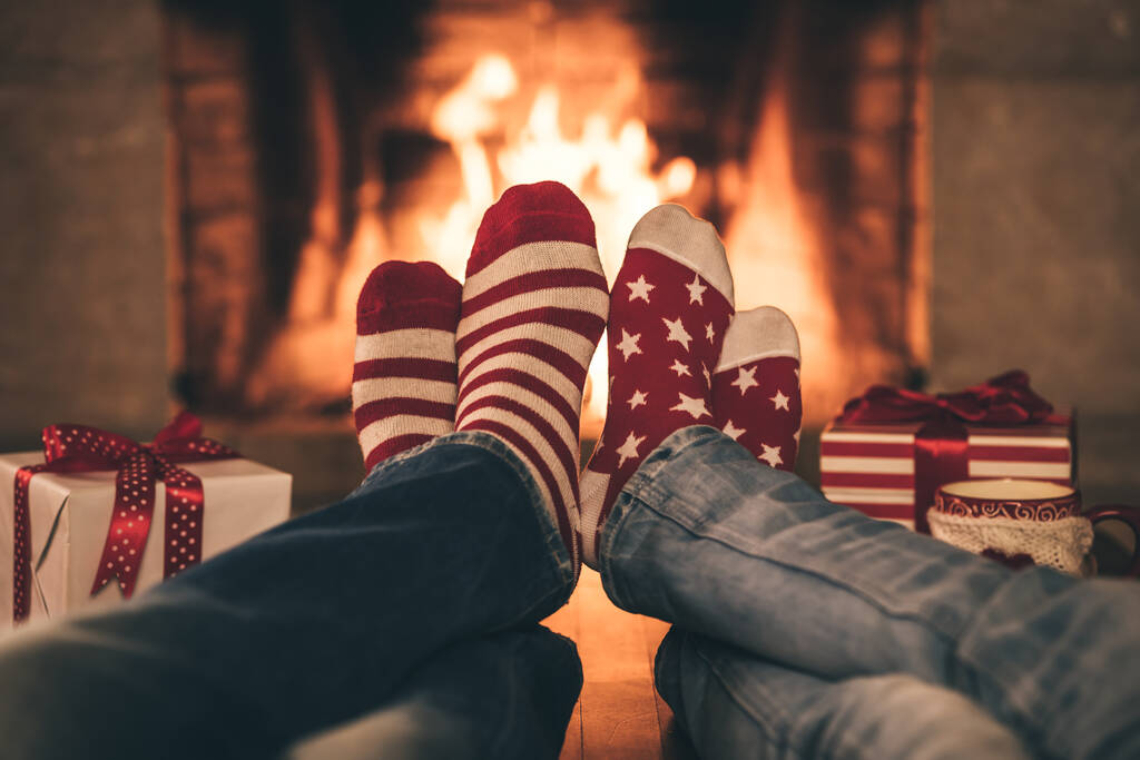 Egy pár karácsonyi zokniban a kandalló mellett. Férfiak és nők jól érzik magukat együtt. Az emberek otthon pihennek. Téli ünnep Xmas és újév koncepció - Fotó, kép