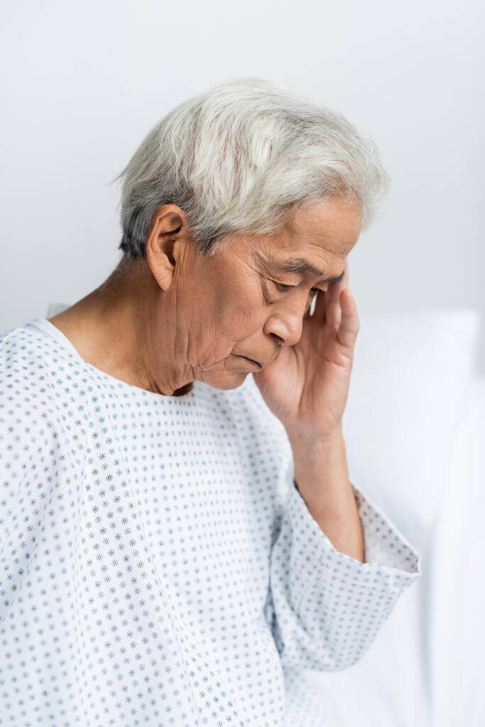 Verontrustende senior aziatische patiënt in toga in ziekenhuis afdeling  - Foto, afbeelding