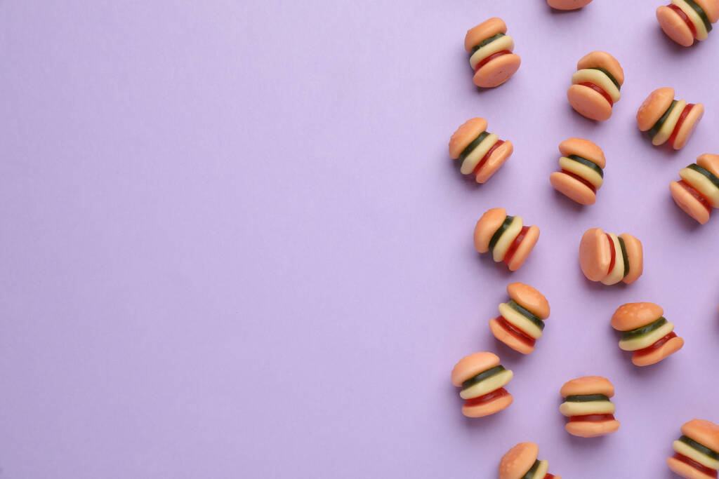 Sabrosos caramelos de gelatina en forma de hamburguesa sobre fondo lila, puesta plana. Espacio para texto - Foto, Imagen