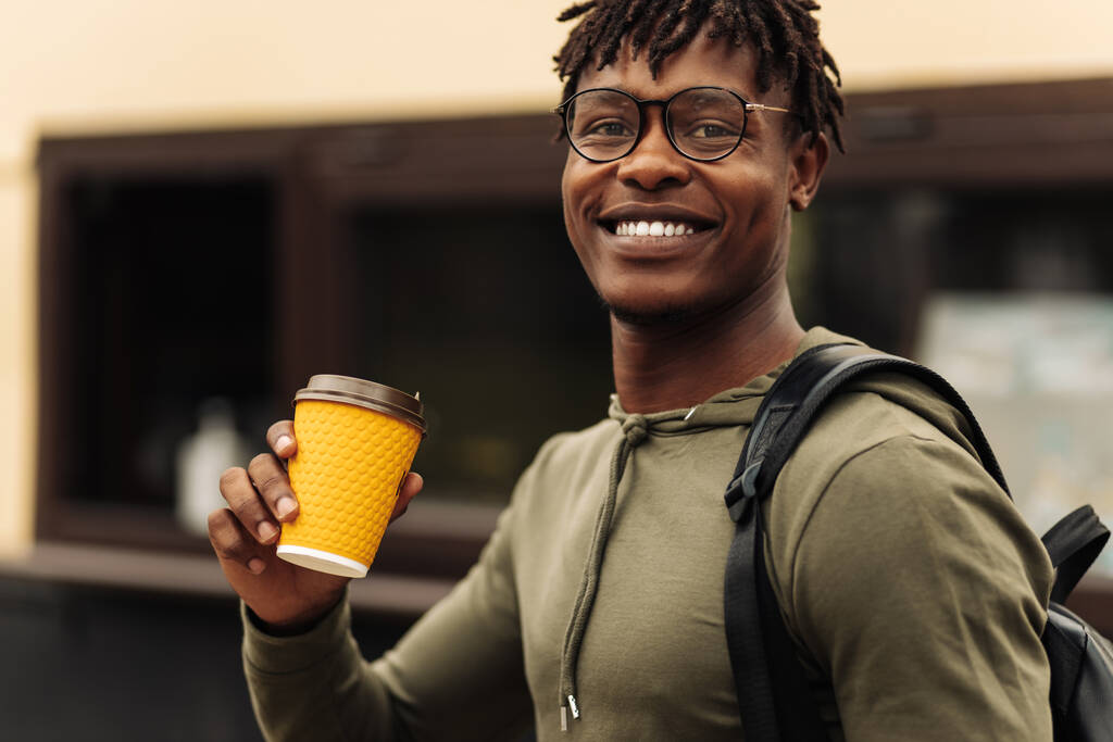 Afbeelding van lachende Spaanse man, met glazen lopen door de stad straat met afhaalkoffie, gelukkige man genieten van warme drank buiten - Foto, afbeelding