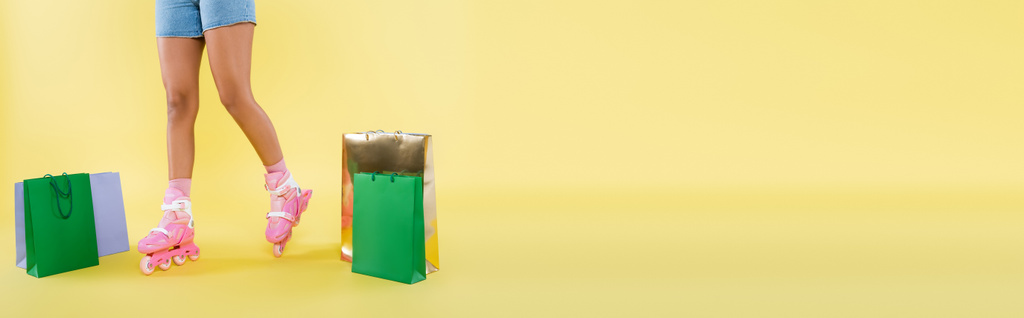 oříznutý pohled na africkou Američanku v kolečkových bruslích v blízkosti nákupních tašek na žluté, banner - Fotografie, Obrázek