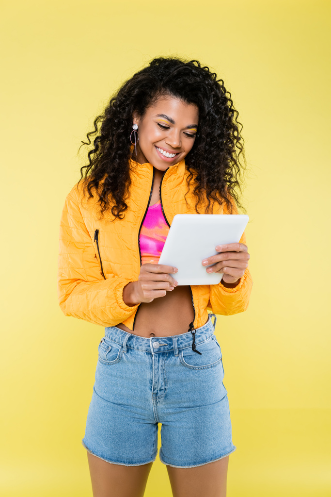 黄色に隔離されたデジタルタブレットを使ってアフリカ系アメリカ人の若い女性を - 写真・画像
