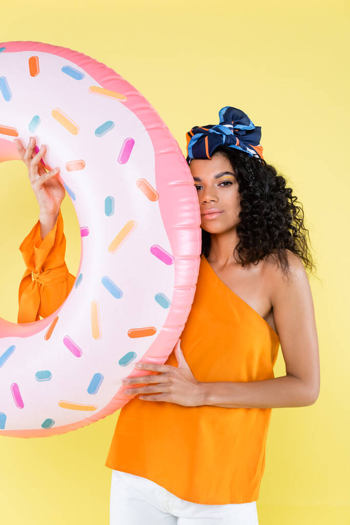 african american young woman in headscarf holding inflatable donut isolated on yellow - Photo, Image