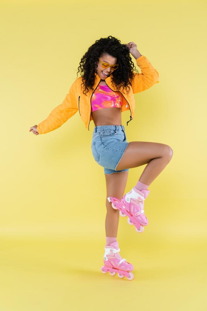teljes hossza boldog és göndör afro-amerikai fiatal nő rózsaszín görkorcsolya sárga - Fotó, kép