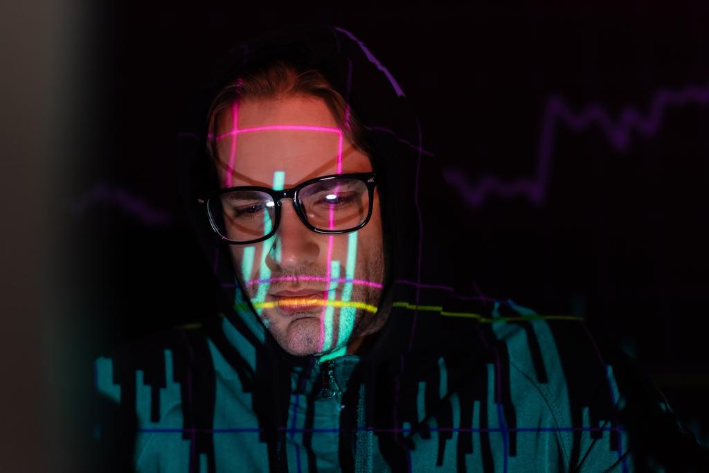 Недовольный хакер с отражением графиков смотрит свысока на черный фон  - Фото, изображение