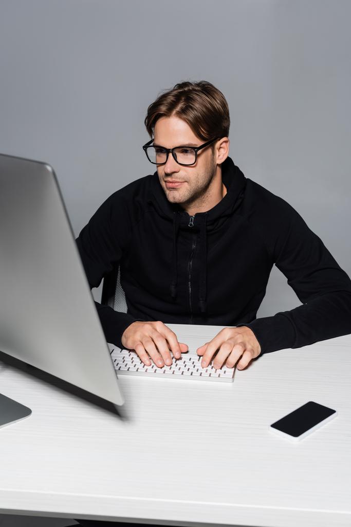 Програміст в окулярах за допомогою комп'ютера біля смартфона ізольовано на сірому
  - Фото, зображення