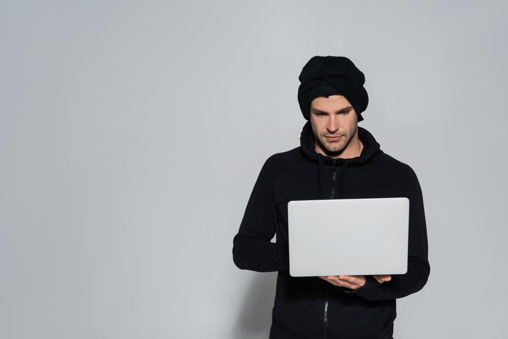Hacker in balaclava using laptop on grey background  - Photo, Image