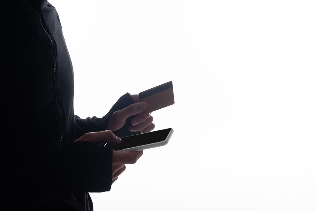Обрізаний вид хакера за допомогою смартфона і тримання кредитної картки ізольовано на білому
  - Фото, зображення