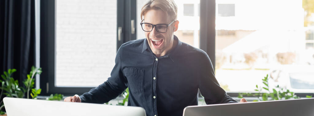 Ενθουσιασμένος προγραμματιστής σε γυαλιά που κοιτάζει οθόνες υπολογιστών στο γραφείο, banner  - Φωτογραφία, εικόνα