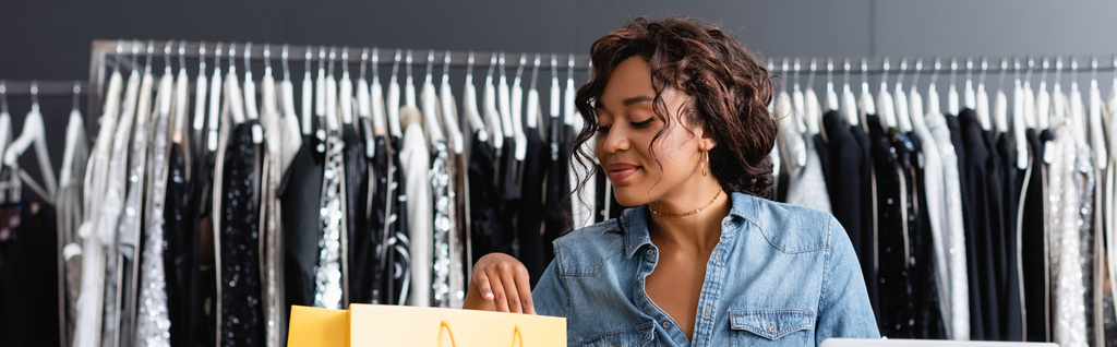 veselá africká americká prodavačka při pohledu na žlutý papírový sáček, banner - Fotografie, Obrázek