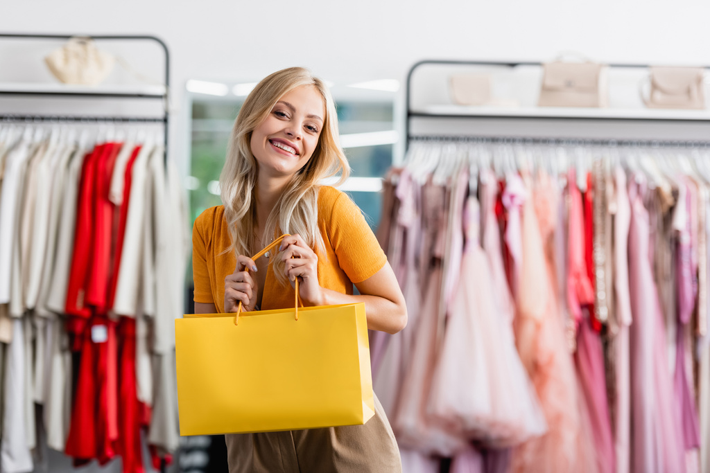 happy woman holding yellow shopping bag in clothing boutique - Photo, Image