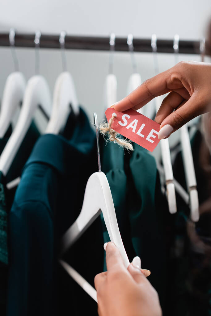 bijgesneden mening van Afrikaanse Amerikaanse verkoopster holding hanger met verkoop tag in kleding boetiek - Foto, afbeelding