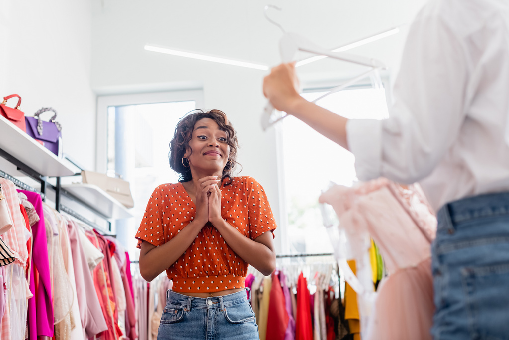 joyful african american woman looking at friend holding pink dress on hanger  - Photo, Image