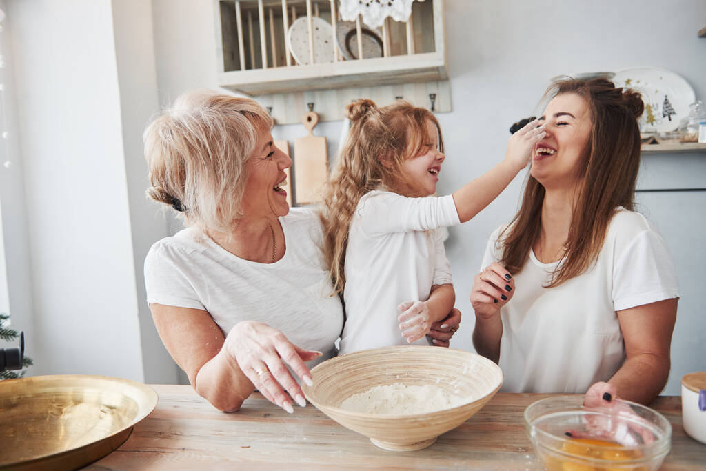 Flour on the nose. Mother, grandmother and daughter having good time in the kitchen. - Photo, Image