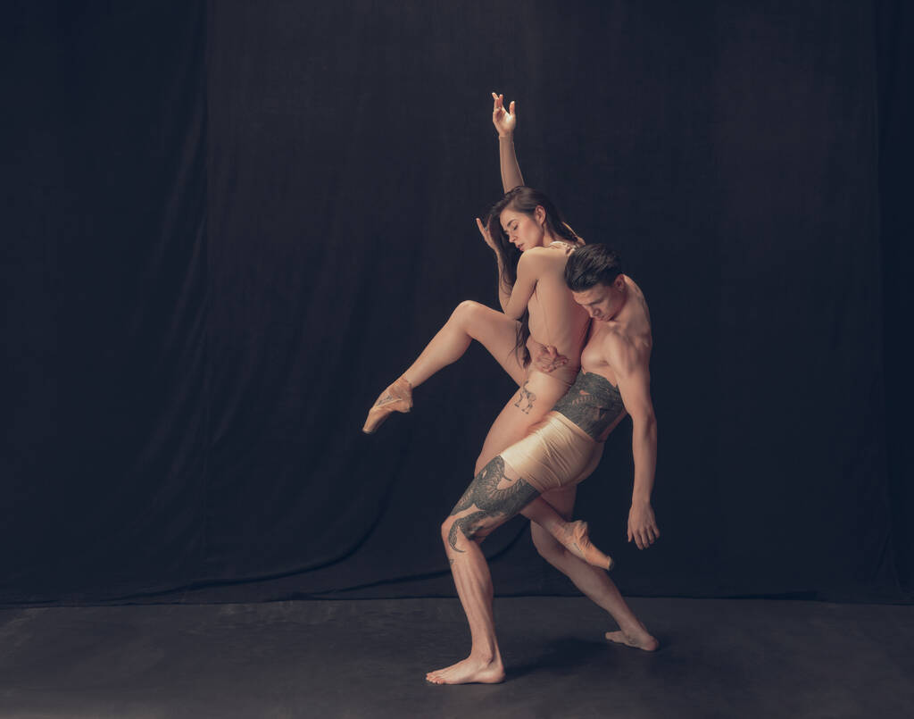 ブラック・スタジオを背景にした現代美術のパフォーマンスでは、 2人の柔軟なダンサー、若い男性と女性が孤立している。芸術、運動、インスピレーションの概念. - 写真・画像