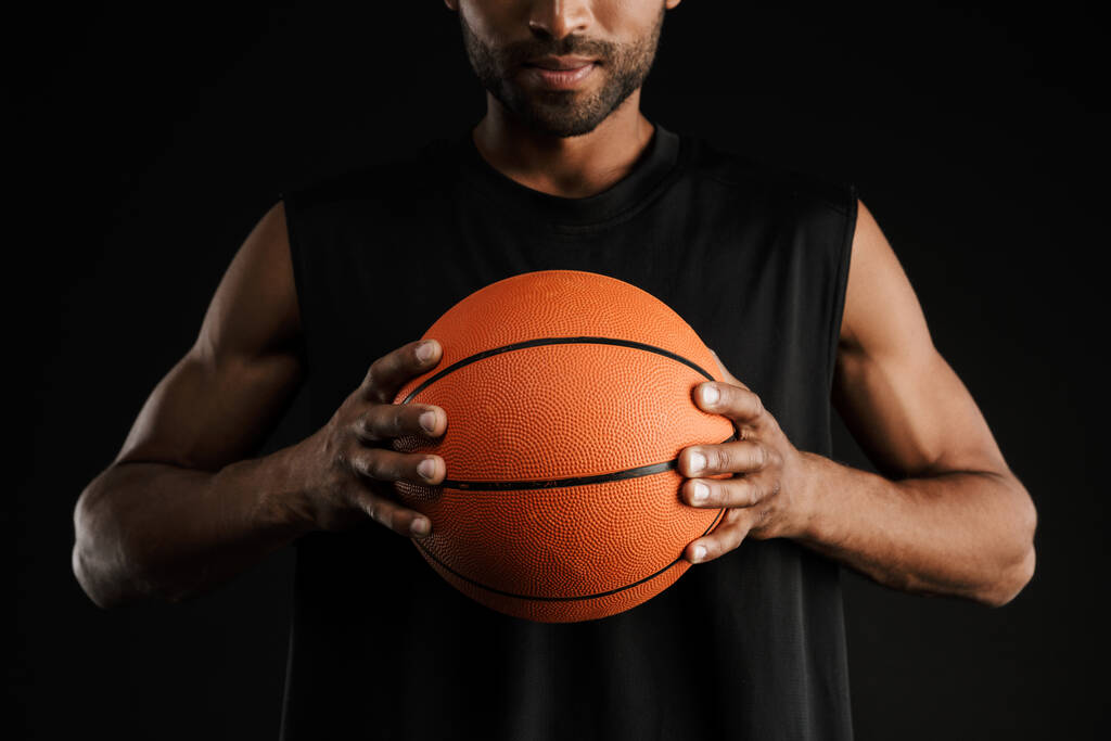 Jovem desportista olhando para a câmera enquanto posando com basquete isolado sobre fundo preto - Foto, Imagem