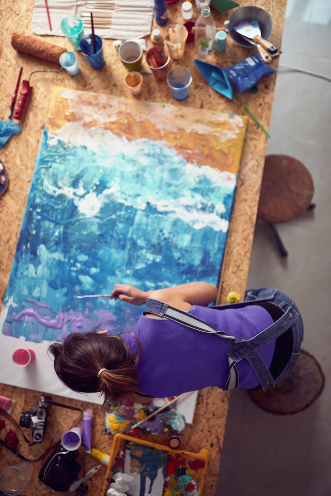 Atölyesinde yaratıcı bir atmosferde resim yapan genç bir kadın sanatçının kuş bakışı görüntüsü. Sanat, resim, stüdyo - Fotoğraf, Görsel