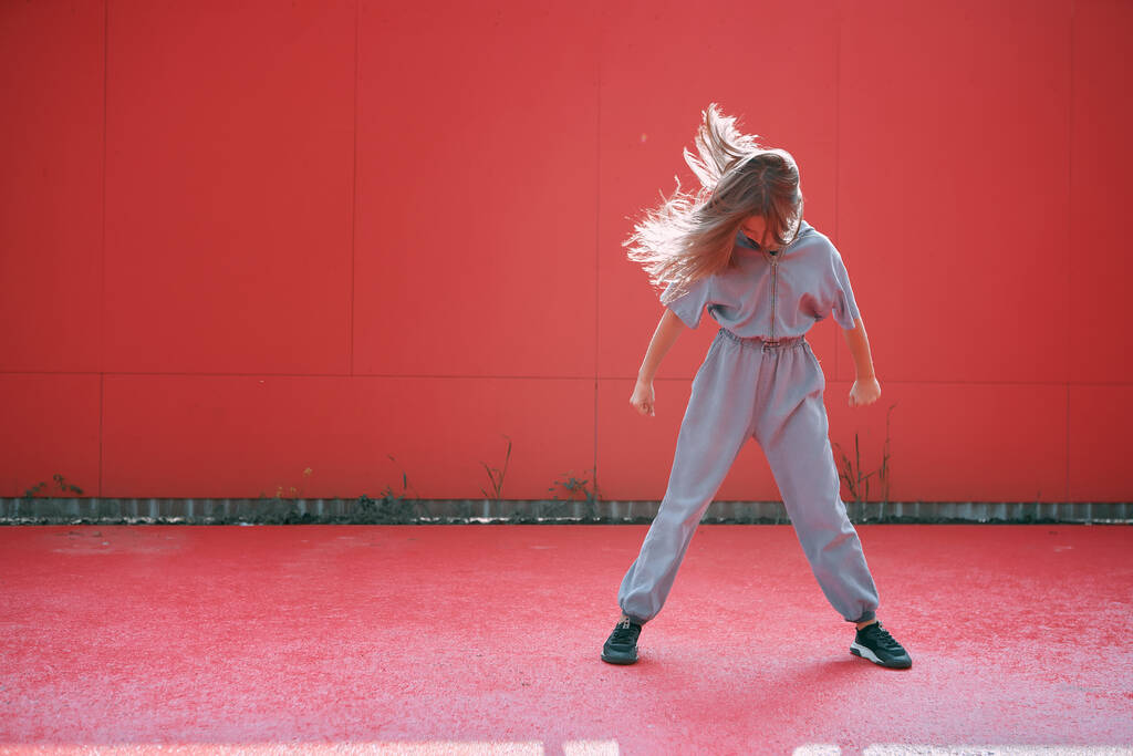 Κομψό ενεργό έφηβο κορίτσι με μακριά κυματιστά μαλλιά φορώντας μοντέρνα ρούχα σε κόκκινο φόντο με χώρο αντίγραφο για διαφήμιση - Φωτογραφία, εικόνα