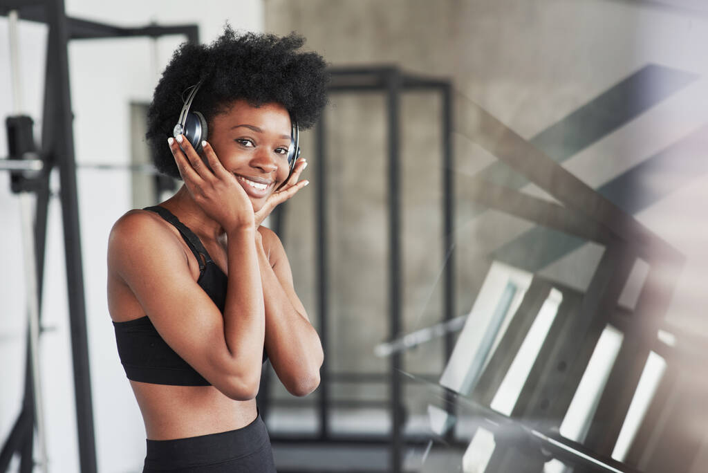 Ωραία αντανάκλαση. Αφροαμερικανή γυναίκα με σγουρά μαλλιά και σπορ ρούχα έχουν fitness day στο γυμναστήριο. - Φωτογραφία, εικόνα