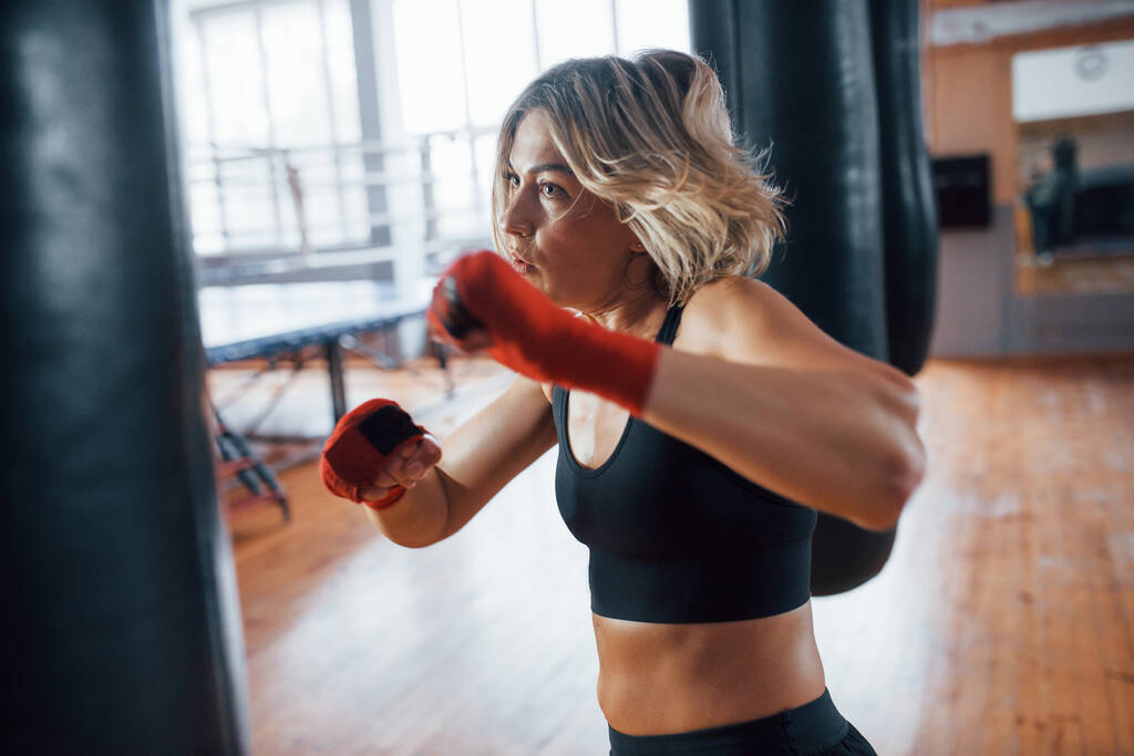 Zelfverdediging. Vrouwelijke bokser slaat op de zak. Blond hebben oefening in de sportschool. - Foto, afbeelding