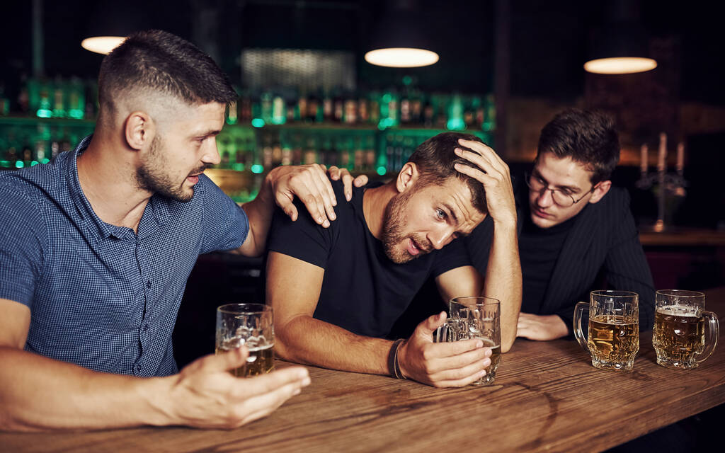 Tres amigos varones en el bar. Apoyando a un amigo triste. Unidad de personas. Con cerveza en la mesa. - Foto, Imagen