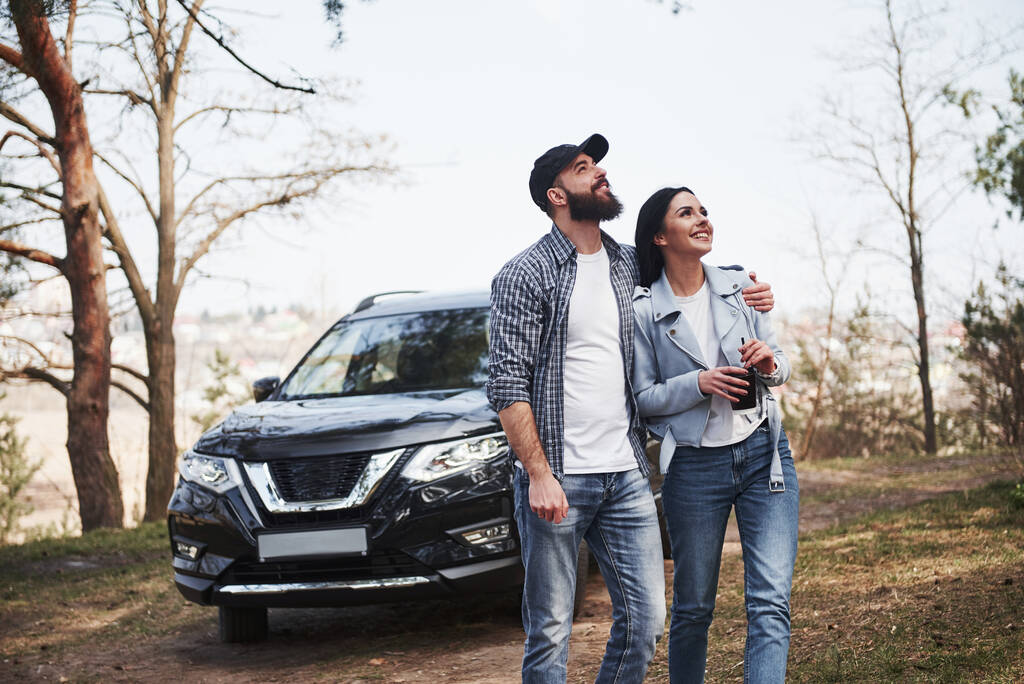 Ready for the new directions. Embracing and enjoying the nature. Couple have arrived to the forest on their brand new black car. - Foto, Imagem