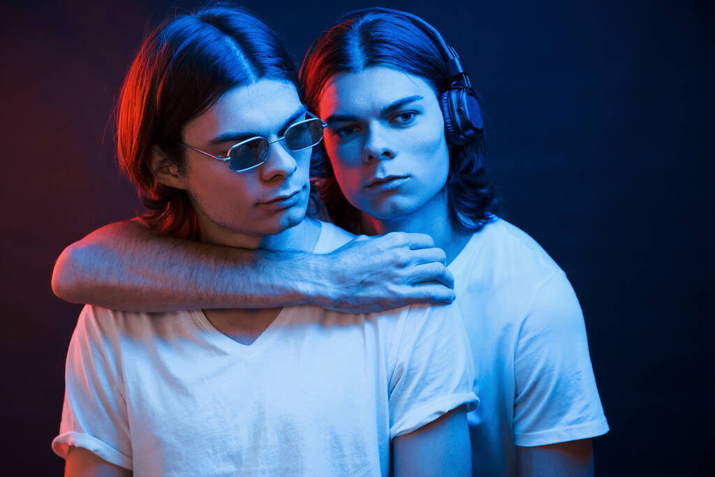 Embracing each other. Portrait of twin brothers. Studio shot in dark studio with neon light. - Photo, Image